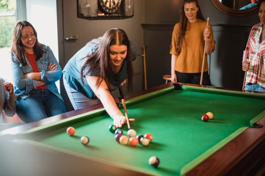 Small group of female friends playing a game of pool in a games room in a house.