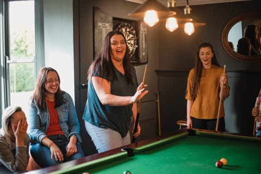 Small group of female friends playing a game of pool in a games room in a house.
