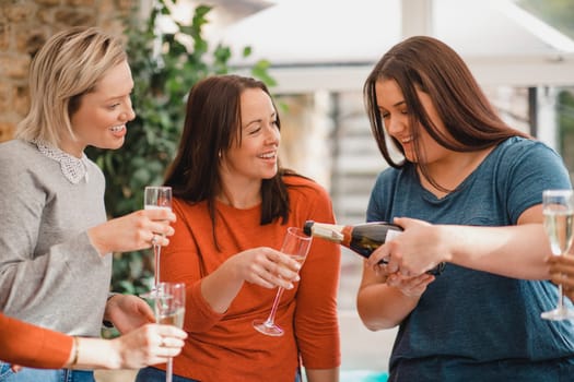 Small group of female friends celebrating at a house party. They are enjoying a glass of champagne, laughing and smiling.