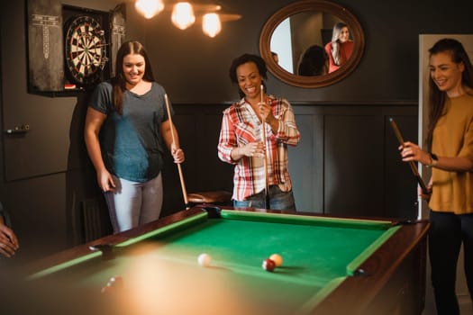 Small group of female friends playing a game of pool in a games room in a house.