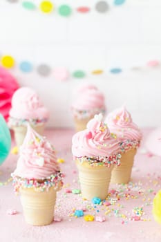 Pink soft serve ice cream with colorful sprinkles in little waffle cups