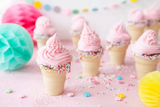 Pink soft serve ice cream with colorful sprinkles in little waffle cups