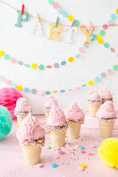 Pink soft serve ice cream with colorful sprinkles in little waffle cups