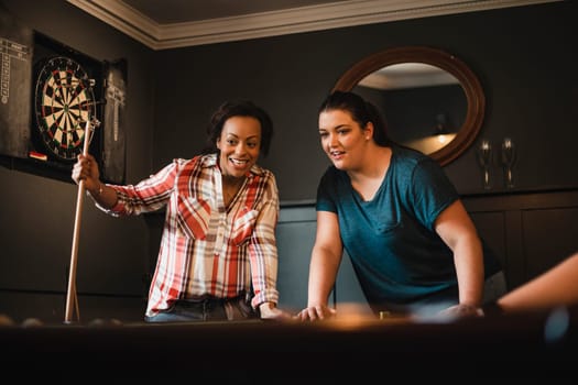 Small group of female friends playing a game of pool in a games room in a house.