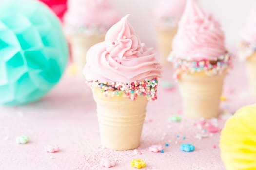 Pink soft serve ice cream with colorful sprinkles in little waffle cups