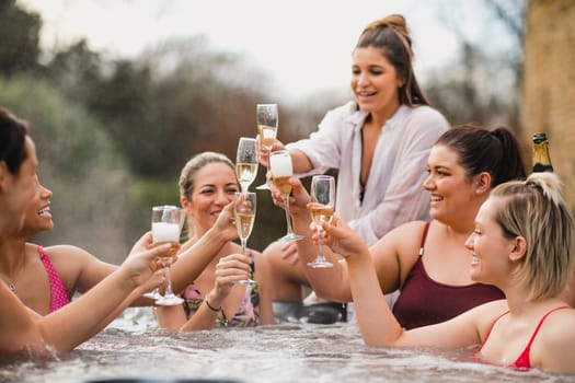 Small group of female friends socialising and relaxing in the hot tub on a weekend away. They are celebrating with a glass of champagne.