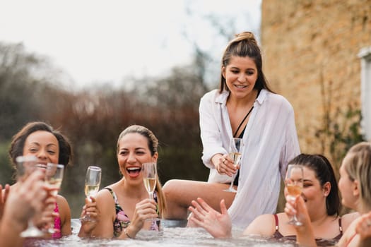 Small group of female friends socialising and relaxing in the hot tub on a weekend away. They are celebrating with a glass of champagne.