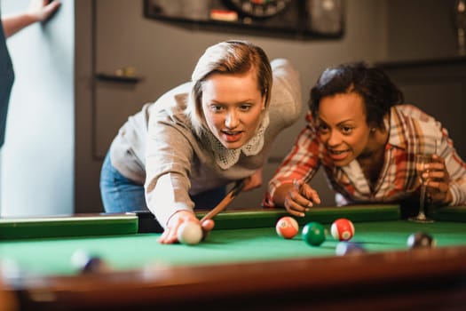 Close-up of two female friends playing a game of pool. They are lining up the shot and practicing.