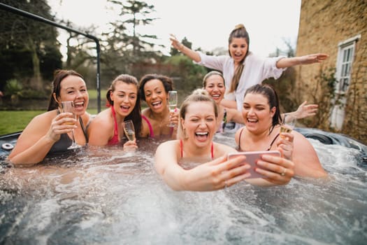 Small group of female friends enjoying a weekend away. They are taking a group selfie while sitting in a hot tub.