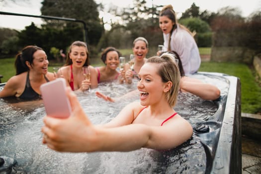 Small group of female friends enjoying a weekend away. They are taking a group selfie while sitting in a hot tub.