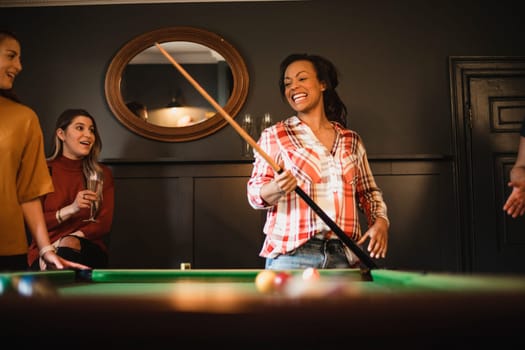 Small group of female friends playing a game of pool in a games room in a house.