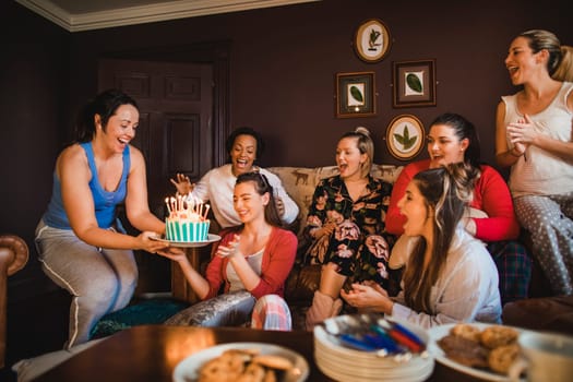 Small group of female friends celebrating a birthday with a Birthday cake while relaxing at home.
