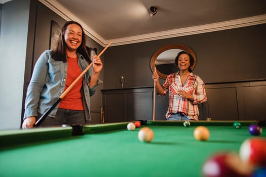 Two mid adult friends playing a game of pool in a games room in a house.