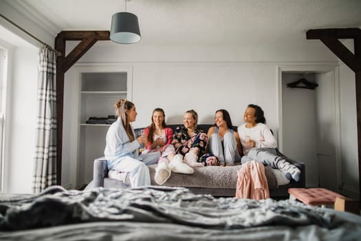 Small group of female friends sitting in a bedroom on a weekend away. They're relaxing in their pyjamas and talking.