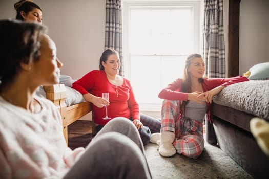 Small group of female friends relaxing and talking while enjoying a girls night in. They are sitting in a bedroom in their pyjamas.