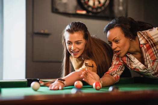 Close-up of two female friends playing a game of pool. They are lining up the shot and practicing.