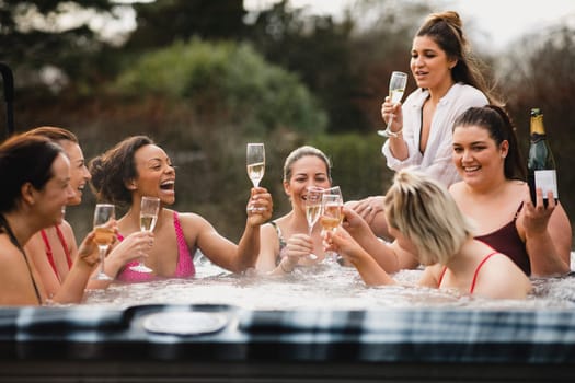 Small group of female friends socialising and relaxing in the hot tub on a weekend away. They are celebrating with a glass of champagne.