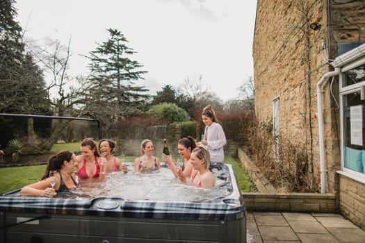 Small group of female friends socialising and relaxing in the hot tub on a weekend away. They are celebrating with a glass of champagne.