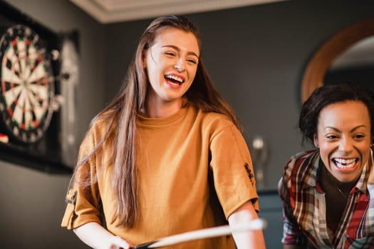 Young female adult having fun and laughing while playing a game of pool with her friend.