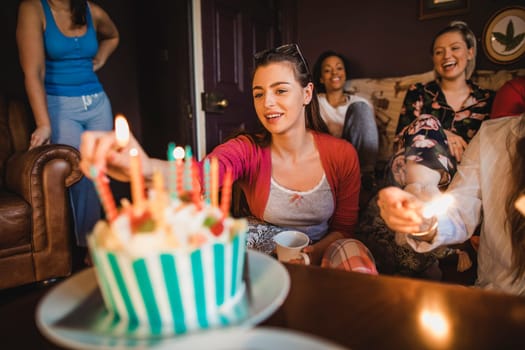 Small group of female friends celebrating a birthday with a Birthday cake while relaxing at home.