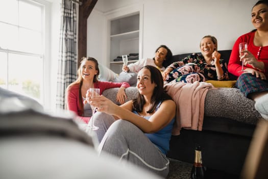 Small group of female friends relaxing and talking while enjoying a girls night in. They are sitting in a bedroom in their pyjamas.