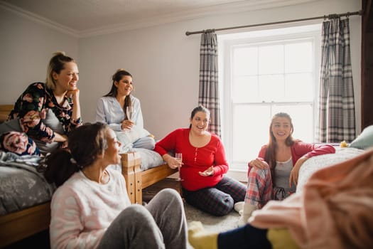 Small group of female friends relaxing and talking while enjoying a girls night in. They are sitting in a bedroom in their pyjamas.