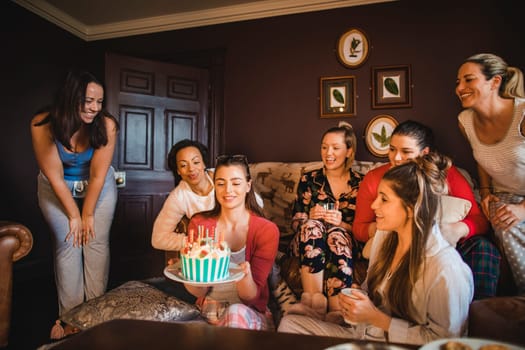Small group of female friends celebrating a birthday with a Birthday cake while relaxing at home.