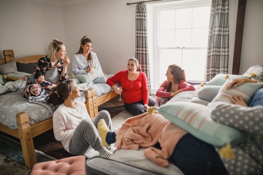 Small group of female friends relaxing and talking while enjoying a girls night in. They are sitting in a bedroom in their pyjamas.