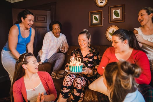 Small group of female friends celebrating a birthday with a birthday cake while relaxing at home.