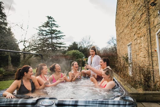 Small group of female friends socialising and relaxing in the hot tub on a weekend away. They are celebrating with a glass of champagne.