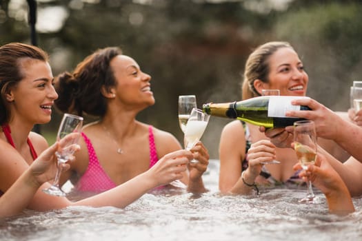 Small group of female friends socialising and relaxing in the hot tub on a weekend away. They are celebrating with a glass of champagne.
