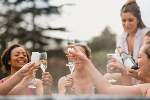 Small group of female friends socialising and relaxing in the hot tub on a weekend away. They are celebrating with a glass of champagne.