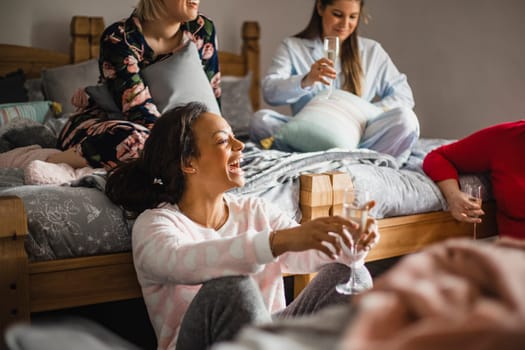 Small group of female friends relaxing and talking while enjoying a girls night in. They are sitting in a bedroom in their pyjamas.