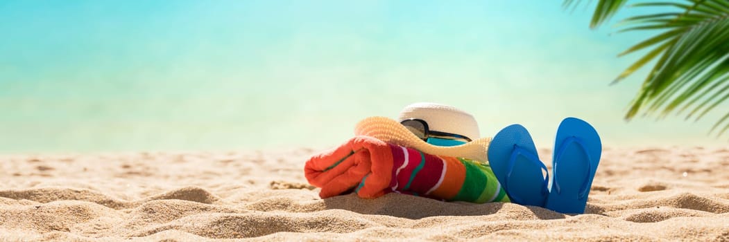 Beach accessories straw hat, flip flops, towel on sunny tropical beach, summer holidays
