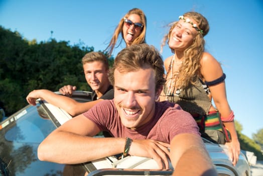 Group of happy people taking a selfie in a car at sunset in summer.