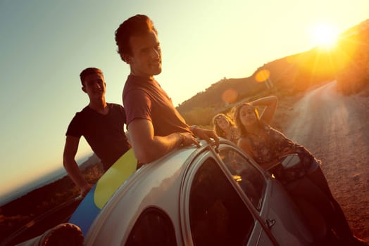 Group of happy people in a car at sunset in summer.