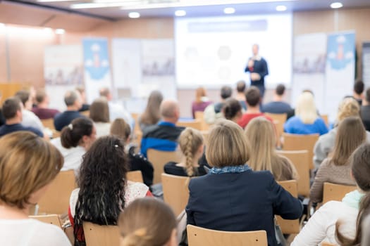 Speaker giving a talk in conference hall at business event. Audience at the conference hall. Business and Entrepreneurship concept. Focus on unrecognizable people in audience.