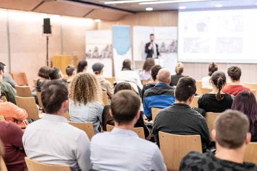 Speaker giving a talk in conference hall at business event. Audience at the conference hall. Business and Entrepreneurship concept. Focus on unrecognizable people in audience.