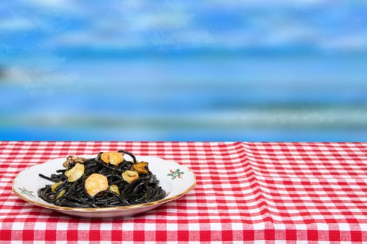 Table top on seafood background. Closeup of mediterranean black noodles with cuttlefish ink, mussels and shrimps on a red checkered tablecloth over abstract blue sky background.