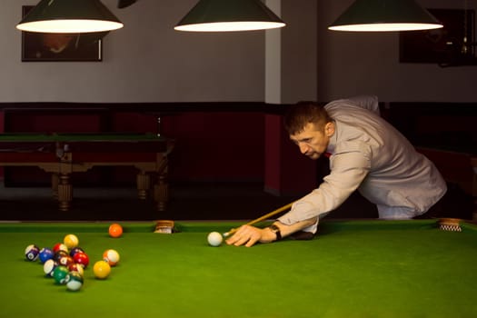 The pool gamer is playing snooker in billiard club indoors.