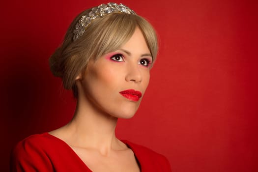 The beautiful elegant fashion model in red dress with tiara is on red background. Fashion portrait.