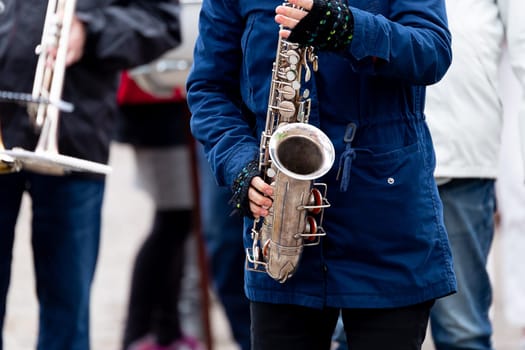 Female Playing Saxohpone Outdoors with a blue jacket.