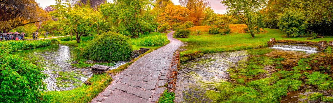enchanted eden garden bridge over pond in horizontal panoramic Nymph Garden or Giardino della Ninfa in Lazio - Italy .
