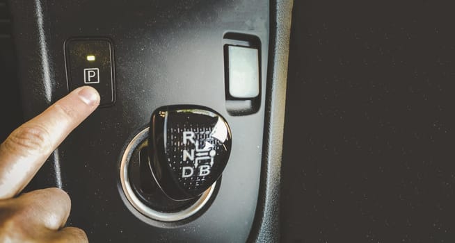hand finger press park gear button on automatic transmission car interior overhead above view horizontal background film grain .