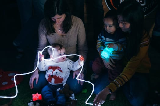 Mother and baby sensory play group are using LED lighting and toys for developmental play.