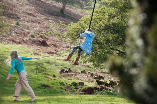 Little girl is being pulled on a monkey swing by her mother.