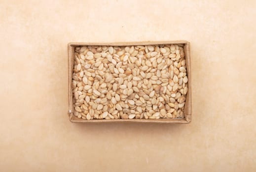 Sesame in small carton on brown background