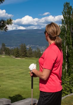 Outdoor photo of female golfer looking at golf course, facing away from camera.