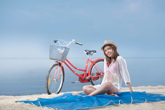 Asian sexy girl with hat sitting on the carpet in beach with bike behind it. Summer vacation