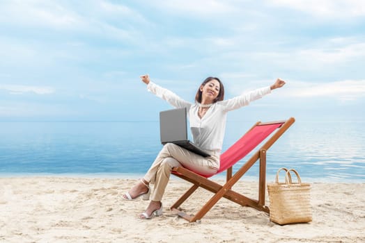 Asian business woman relax when working with laptop sitting in the beach chair on beach. Summer vacation